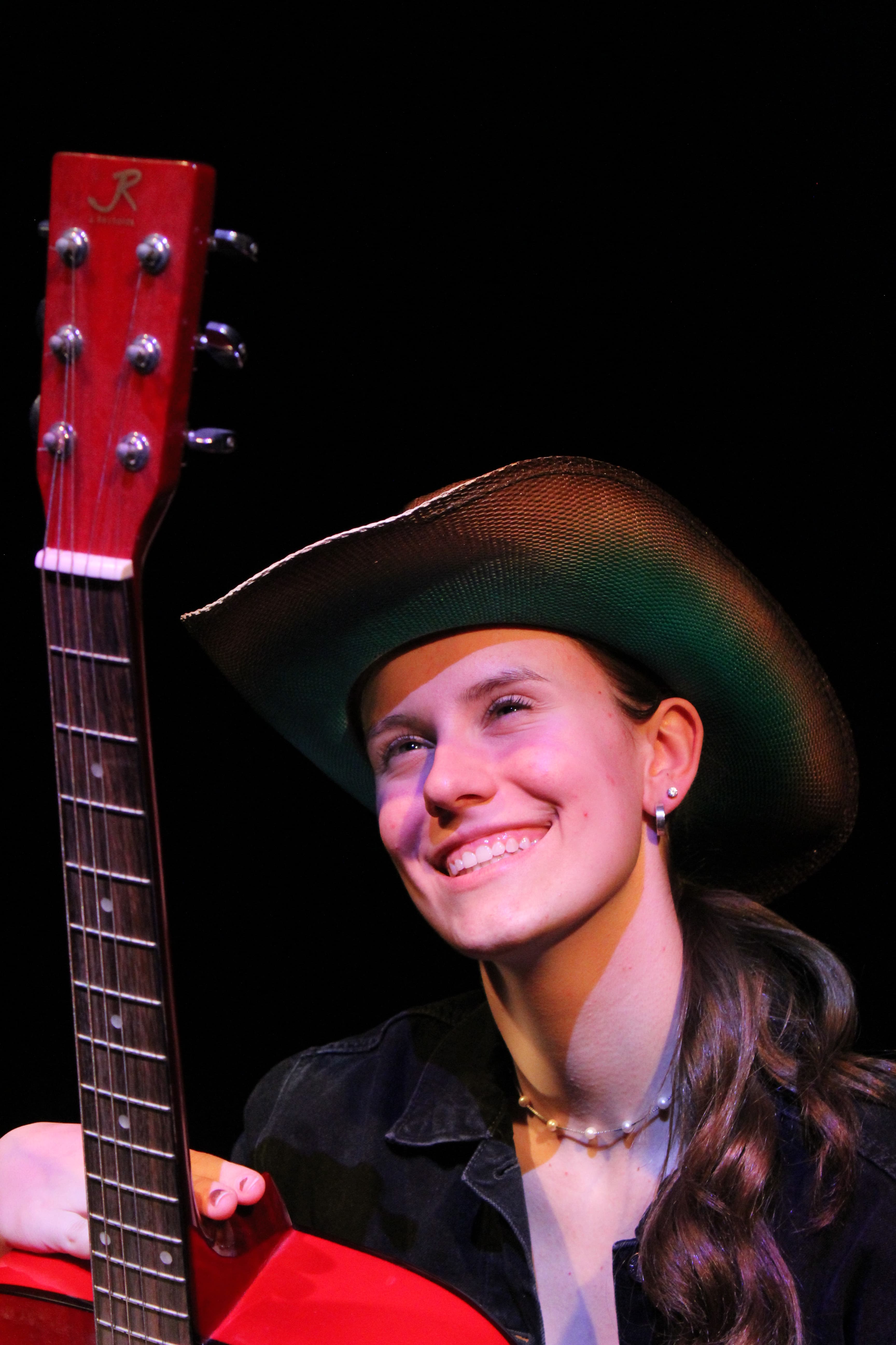 Maya smiling on stage with a guitar