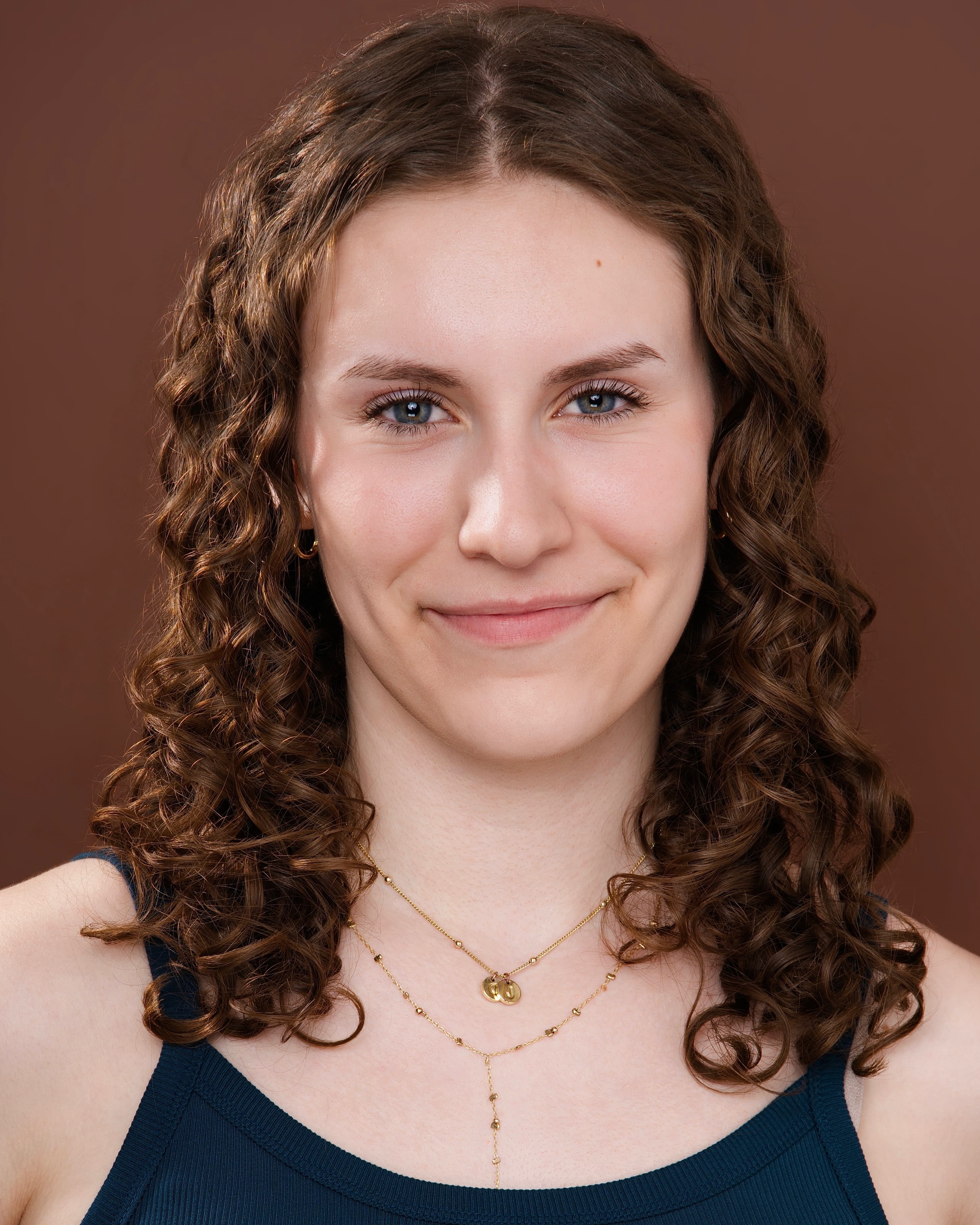 Maya Cassell headshot on a warm maroon backdrop