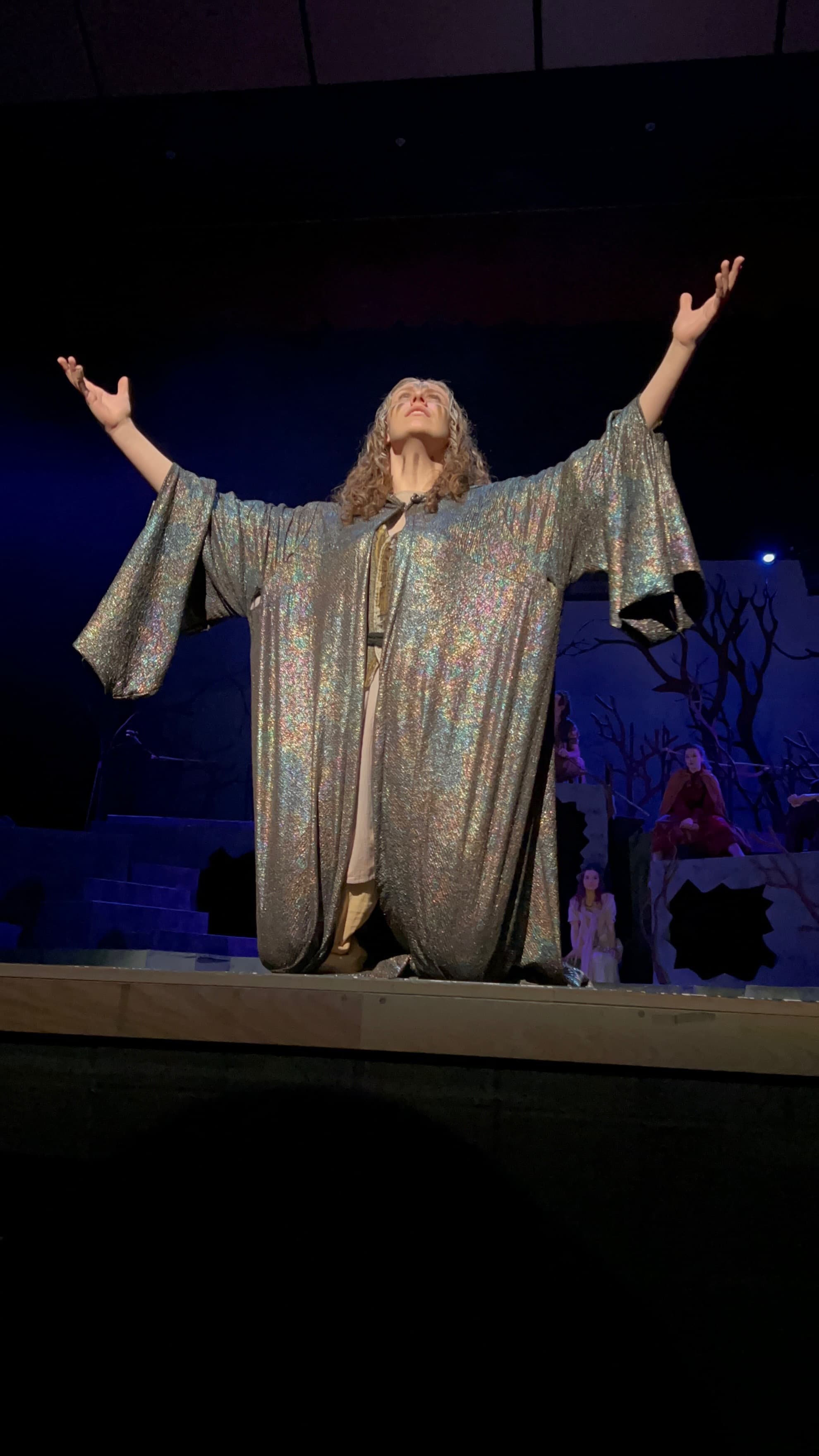 Maya performing in a stage robe with arms raised